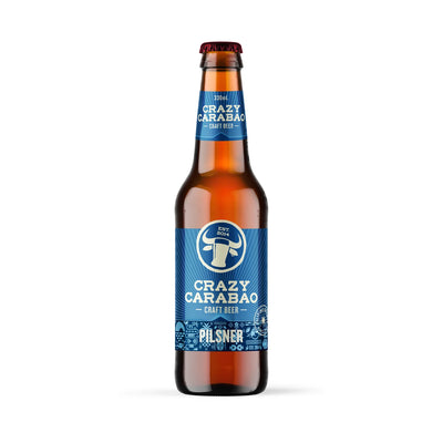 A single bottle of Craft Beer by Crazy Carabao, Cilsner, in a brown glass bottle with a blue label and a red cap, centered on a white background.